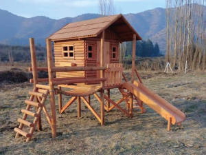 Casas de madera para niños modelo Conguillio elevada con cabaña de troncos, terraza, puente de madera y resbalín.