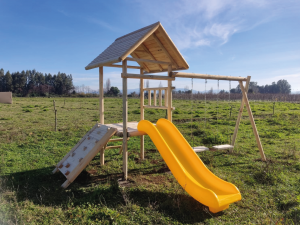 Juegos infantiles para exterior modelo Curicó con torre techada, resbalín amarillo, muro de escalada y dos columpios.