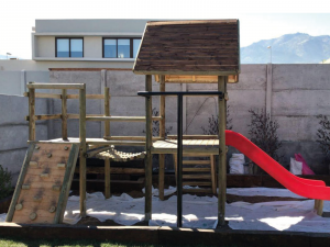 Estructuras de madera para niños modelo Valdivia con torre techada, puente de equilibrio y resbalín rojo.