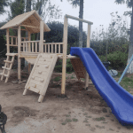 Juegos infantiles de madera modelo Linderos con resbalín azul y muro de escalada frontal.